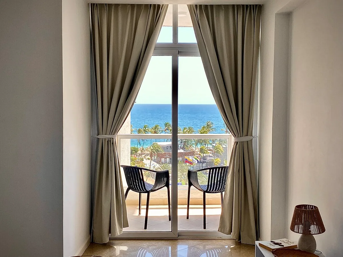 Puerta del dormitorio al balcón con sillas y vista al mar en Pampatar